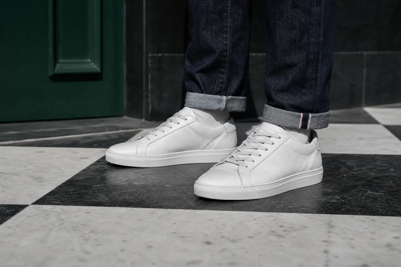 White leather sneakers worn with cuffed dark denim